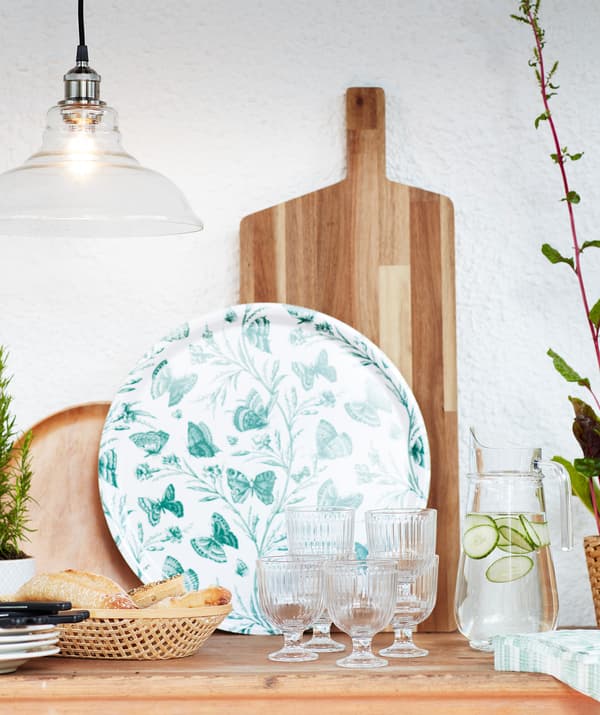 Une table prête pour le dîner, couverte de verres, de pain, de serviettes, d’assiettes, un plateau vert et une planche à découper en bois.