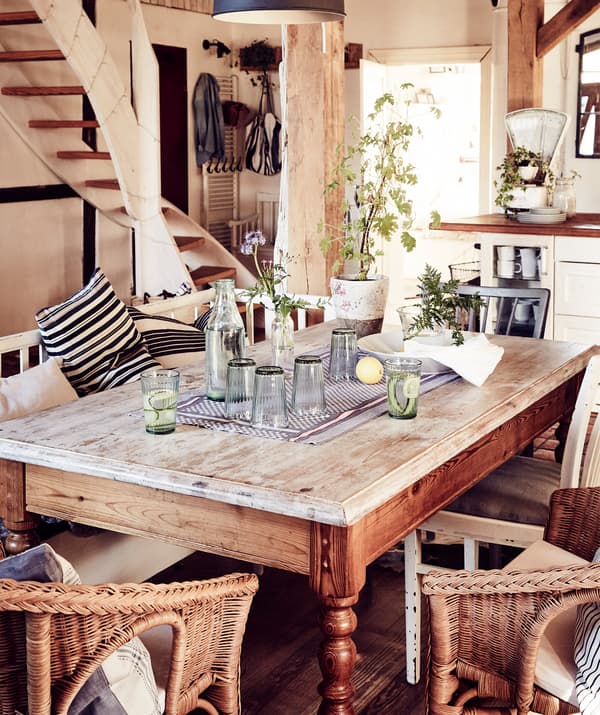 Une table vintage en bois avec des fauteuils en rotin dans un espace de vie décloisonné.