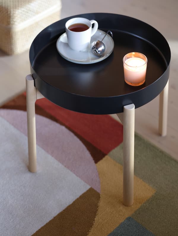 Une tasse de thé et une soucoupe posées sur une table d’appoint YPPERLIG. Une bougie allumée crée une ambiance cosy.