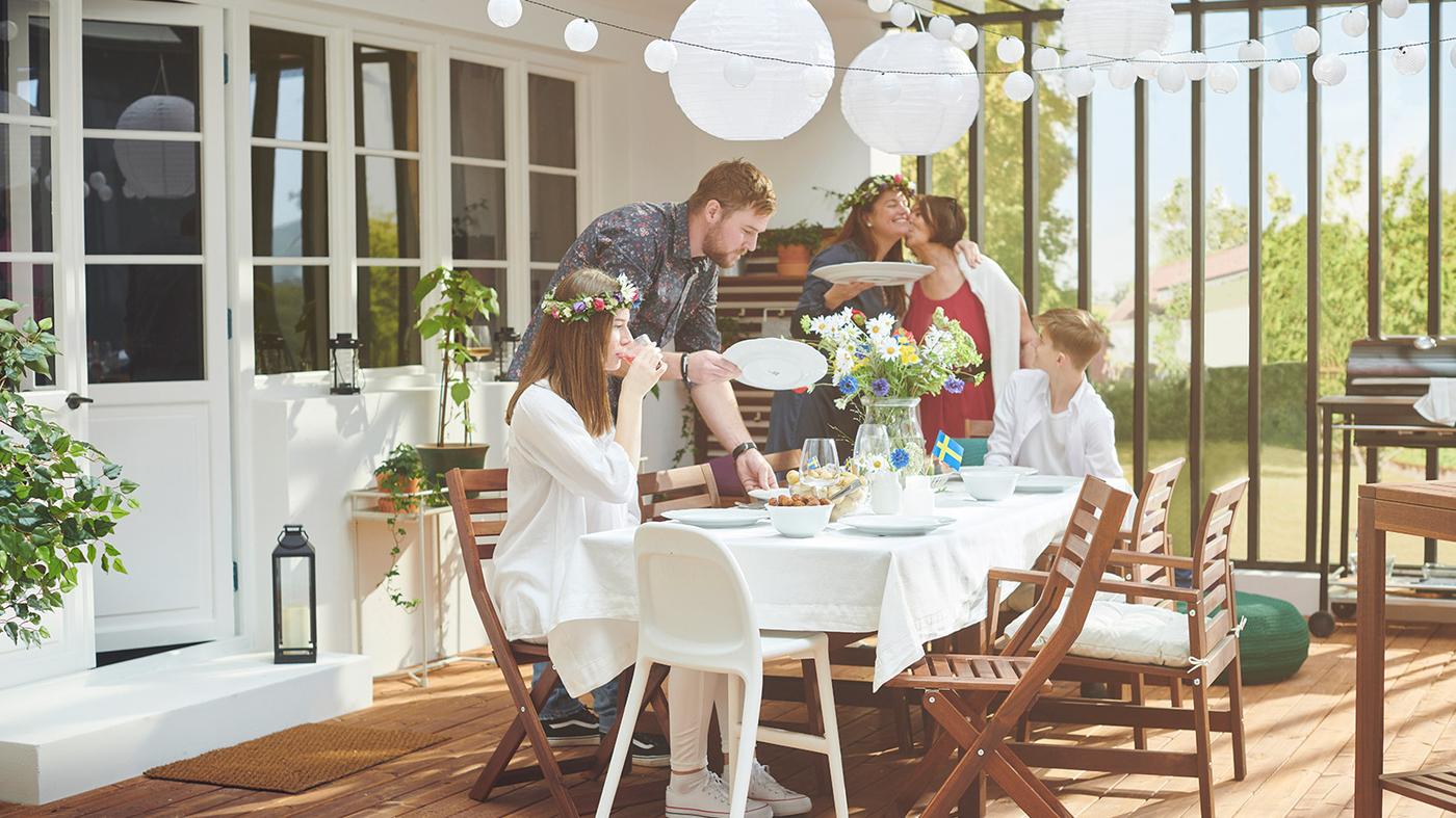Une terrasse couverte ensoleillée avec des gens autour d’une table ornée de fleurs, de lanternes suspendues et d’un petit drapeau suédois.