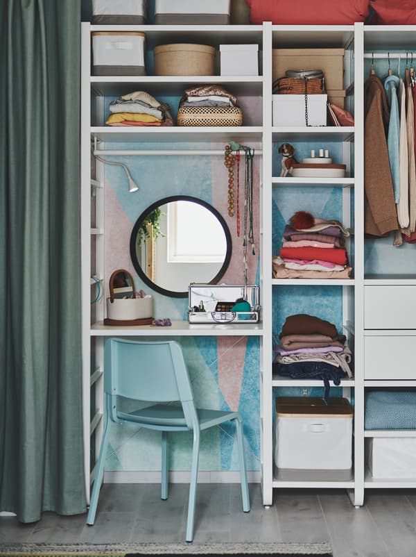 Une unité de rangement couvrant tout le mur en guide de garde-robe, une partie étant utilisée comme coiffeuse, avec un miroir, une chaise TEODORES et du maquillage.
