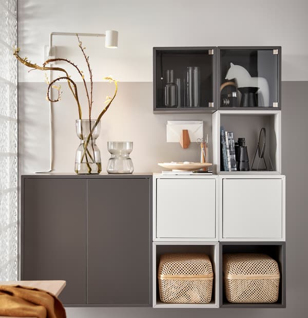Une unité de rangement EKET blanche et grise avec deux boîtes de rangement SMARRA, deux vases en verre et des articles personnels exposés.