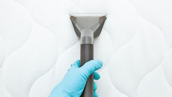 une vue rapprochée d’une personne qui passe l’aspirateur sur un matelas