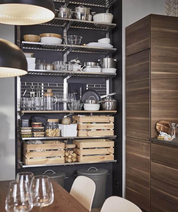 Ustensiles de cuisine, vaisselle et cageots en bois disposés sur un meuble de rangement en métal ouvert contre un mur foncé.
