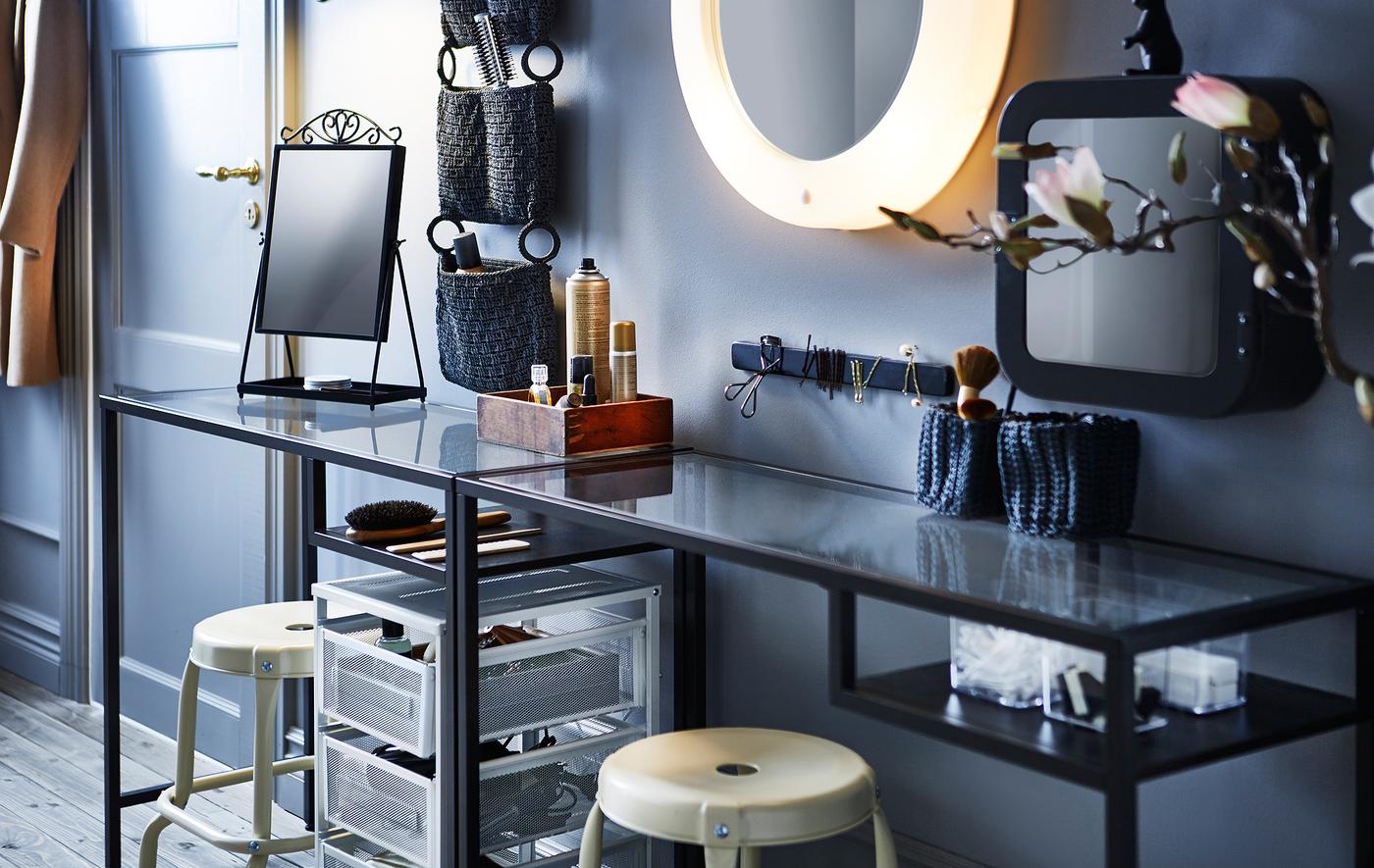 Utilisez une table étroite, deux tabourets, quelques organiseurs, des dessertes et un miroir éclairé pour créer un petit coin coiffeuse.