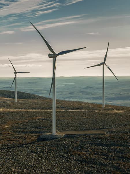 Varios aerogeneradores altos sobre un paisaje montañoso aprovechando la potencia del viento bajo un cielo con nubes.