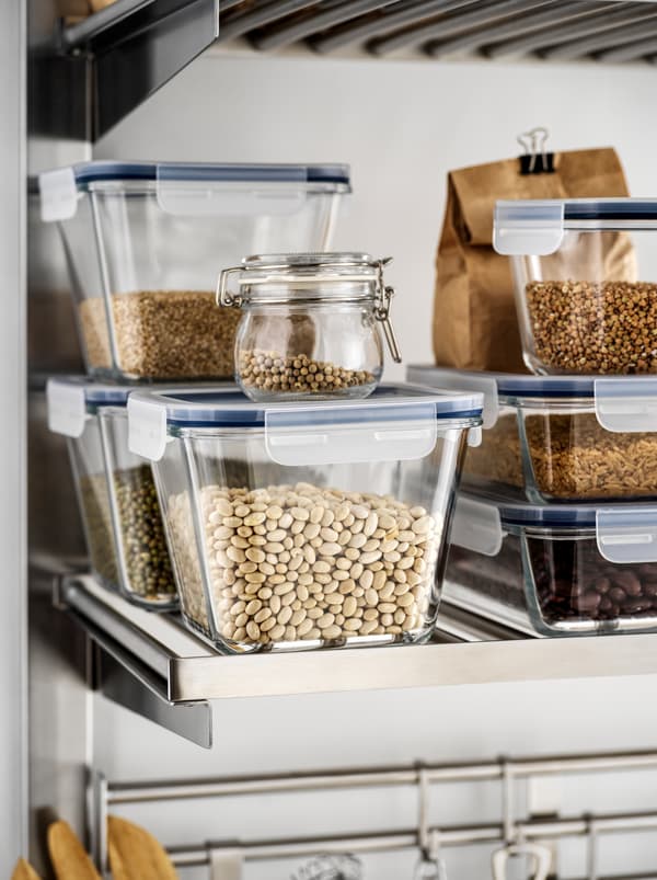 Various dry goods – beans, lentils, grains – in IKEA 365+ glass food containers stacked on a metal kitchen shelf.