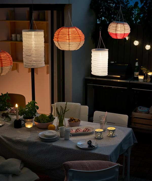 Various shaped IKEA SOLVINDEN solar-powered pendant lamps set up over an outdoor dining table
