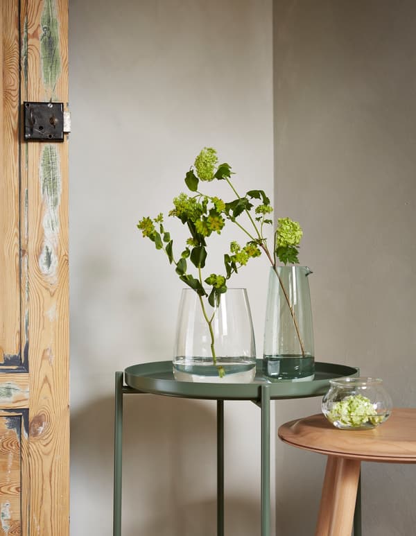 Vases BERÄKNA et VILJESTARK sur une table, avec une plante solitaire et une branche de bourgeons, montrant que les choses simples peuvent être belles.