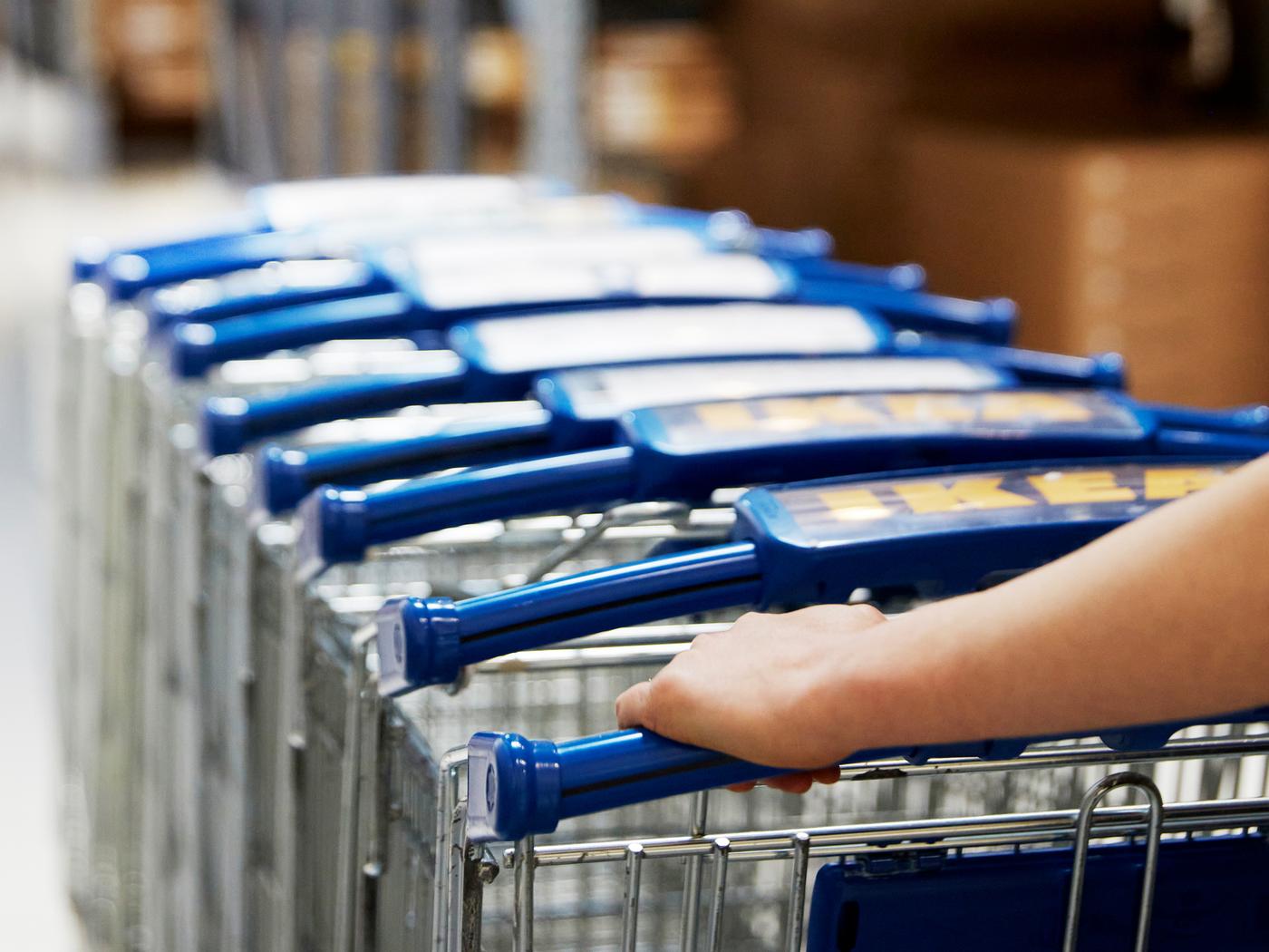 Več nakupovalnih vozičkov IKEA, ki jih nekdo potiska po trgovini IKEA.