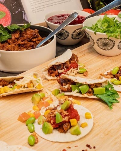 Vegan tacos on a chopping board next to it bowls with sauce, salad, plant based meat