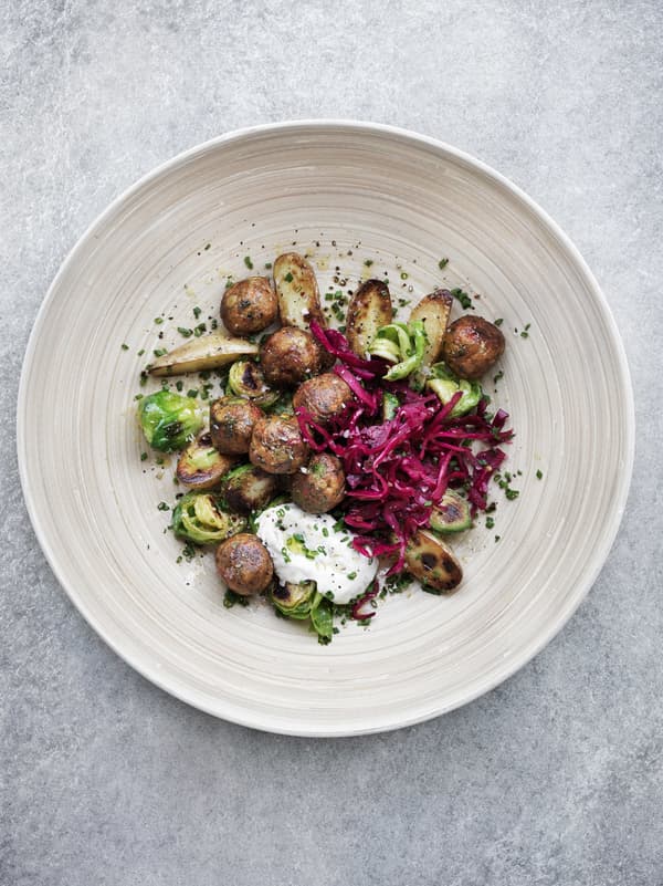 Veggie balls with Brussels sprouts and pickled red cabbage served on a wooden plate, seen from above.