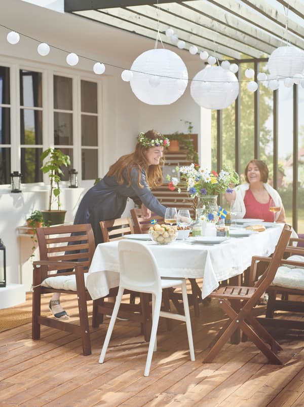 Veranda con due persone attorno a un tavolo ÄPPLARÖ apparecchiato per la festa, circondato da sedie della stessa serie - IKEA