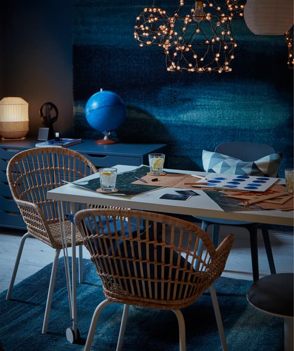 Verres et cartes du ciel sur une table, chaises en osier, guirlande lumineuse à DEL, tapis SÖNDERÖD au sol et au mur.