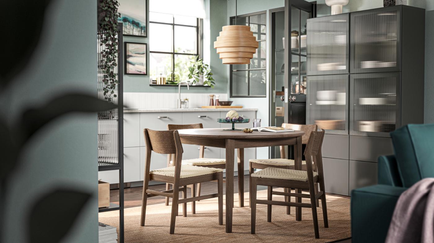 Vier SKANSNÄS Stühle in brauner Buche stehen um einen runden SKANSNÄS Ausziehtisch in brauner Buche/Furnier auf einem flach gewebten LOHALS Teppich.