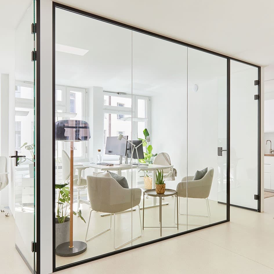 View into an office with glass partition with meeting chairs and two desks in the background