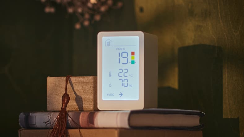 VINDSTYRKA air quality placed on top of a book on a nightstand next to a small wooden container