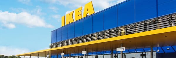 Внешний вид магазина IKEA с большой жёлтой вывеской IKEA на синем здании на фоне частично облачного неба.

