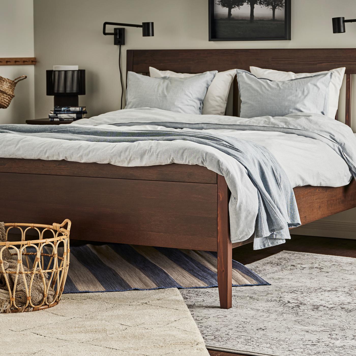 VRENSTED, VEDBÄK and TVERSTED rugs under a dark brown bed made with blue/striped bed linen and a light blue bedspread.