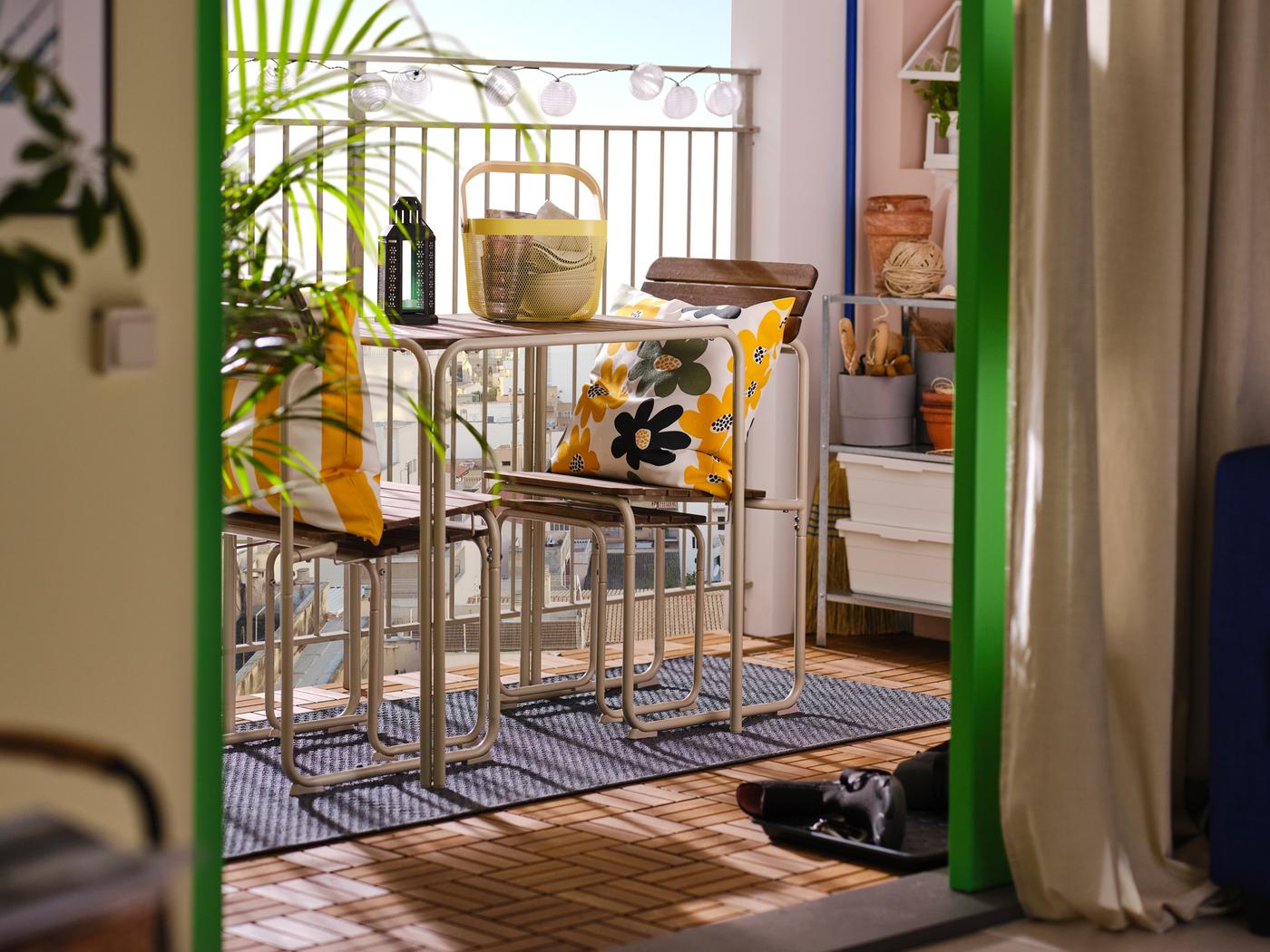 Vu depuis un salon, un balcon avec une table, 2 chaises et 2 repose-pieds FURUÖN, ainsi que des coussins colorés.