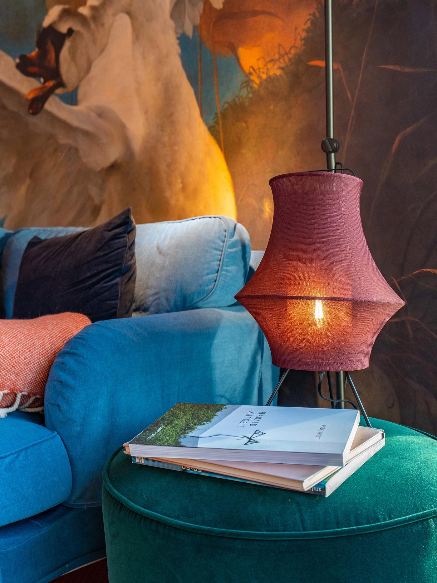 Vue détaillée d’une table d’appoint cylindrique en tissu avec des livres posés dessus et une lampe avec un abat-jour en tissu au-dessus
