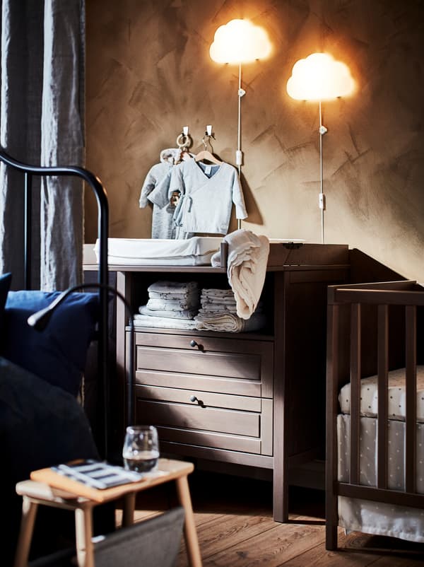 Vue partielle d’une chambre à moitié cachée par un rideau servant de séparateur, avec un lit bébé et une table à langer SUNDVIK.
