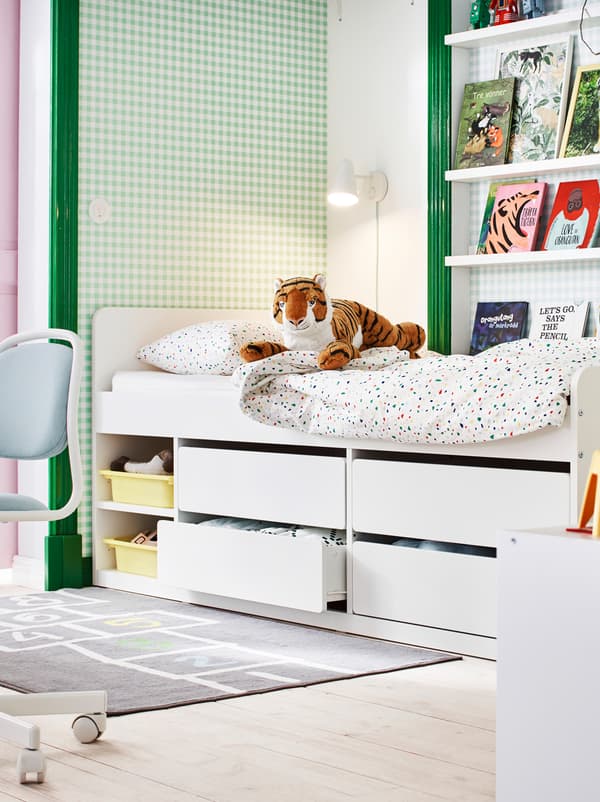 Vue partielle d’une chambre d’enfants en vert et blanc, avec des livres sur des tablettes pour photos, des jouets et un lit SLÄKT avec rangement en-dessous.