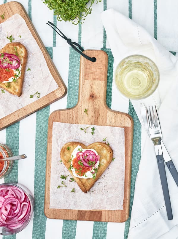 Waffle hearts topped with caviar, creme fraiche and pickled red onion sit on small chopping boards.