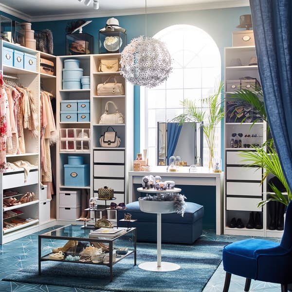 Walk-in closet with white PAX clothes storage shelves, with blue KIVIK footstool and REMSTA dark blue armchair.