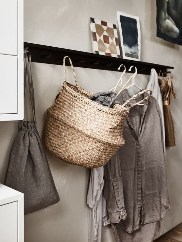 Wall hooks holding clothes on hangers plus a basket.