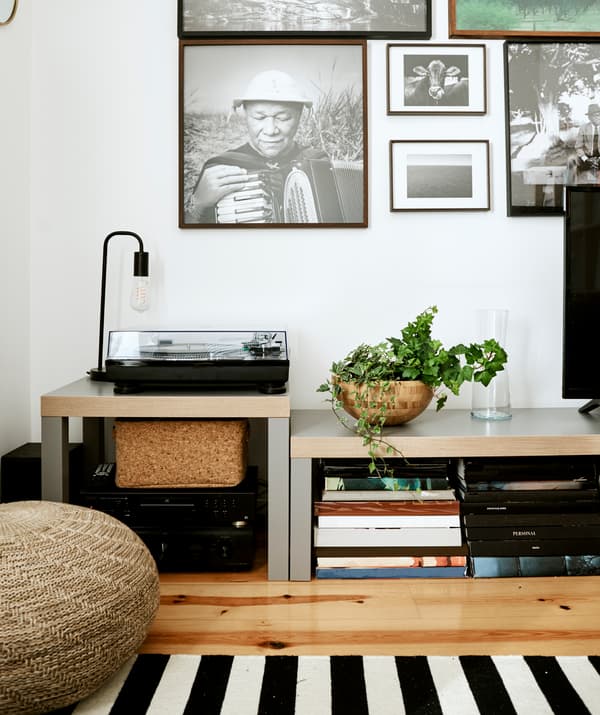 Wall of black and white photos above two low benches, one has a record player, the other has stacks of books beneath it.