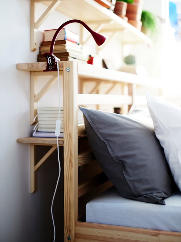 Wall shelves fill the space between a wall and the head end of a bed, creating a combination of storage and bedside table.
