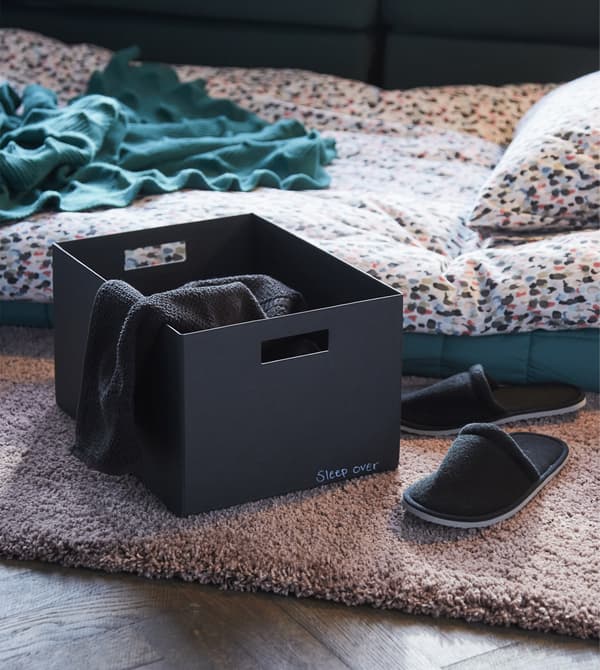 Want home decor ideas that make your place a friend magnet? Prepare for sleepover guests. Collect an extra blanket, slippers and ear plugs in a box like this black TJENA box with lid from IKEA.