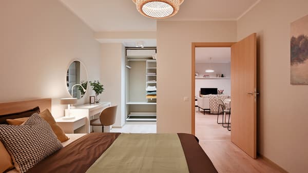 Warm and contemporary bedroom with soft neutral tones, layered textiles, a compact dressing area, and natural wood finishes creating a calm and comfortable atmosphere connected to the open-plan apartment interior.