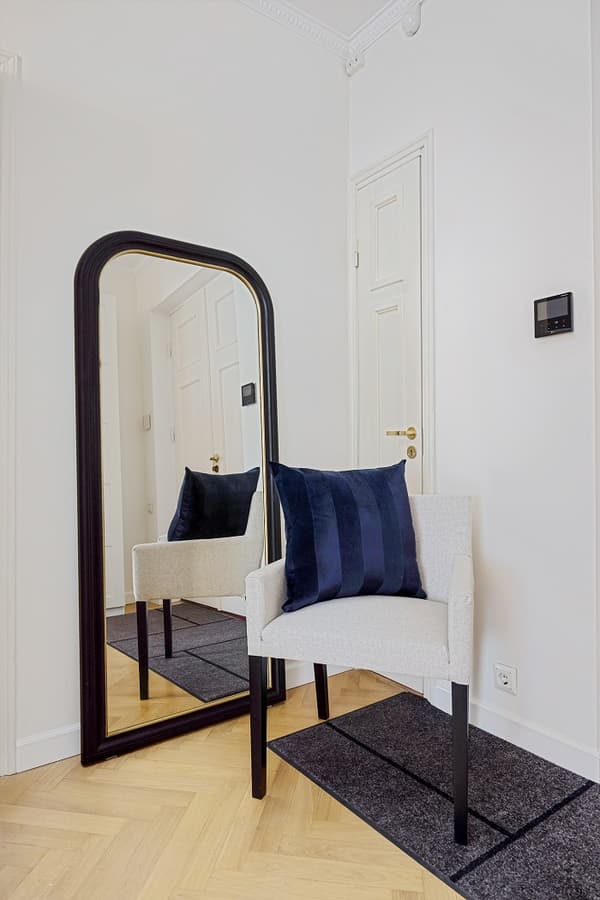White chair with navy cushion placed in front of tall mirror in hallway