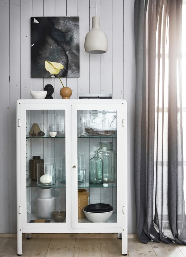 White glass cabinet with pottery and glassware inside.