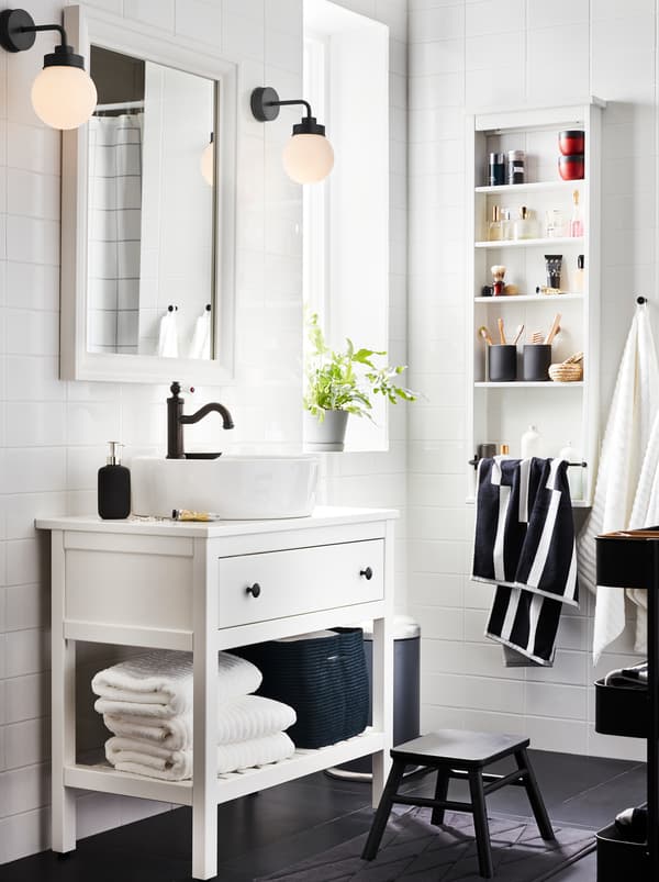 White HEMNES bathroom furniture with one drawer, one shelf with towels and a HAMNSKÄR mixer, a mirror, and two lamps.