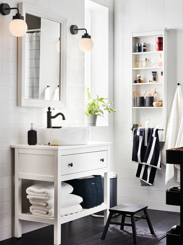 White HEMNES bathroom furniture with one drawer, one shelf with towels and a HAMNSKÄR mixer, a mirror, and two lamps.