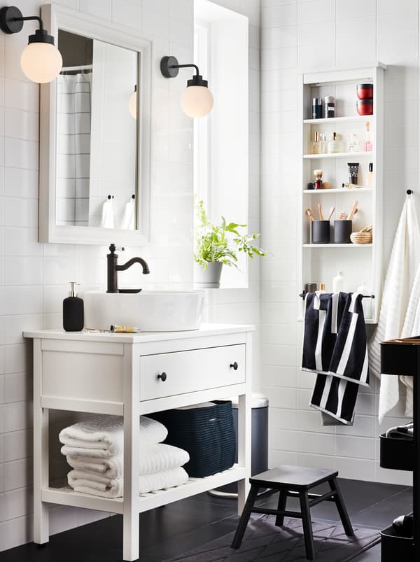 White HEMNES bathroom furniture with one drawer, one shelf with towels and a HAMNSKÄR mixer, a mirror, and two lamps.
