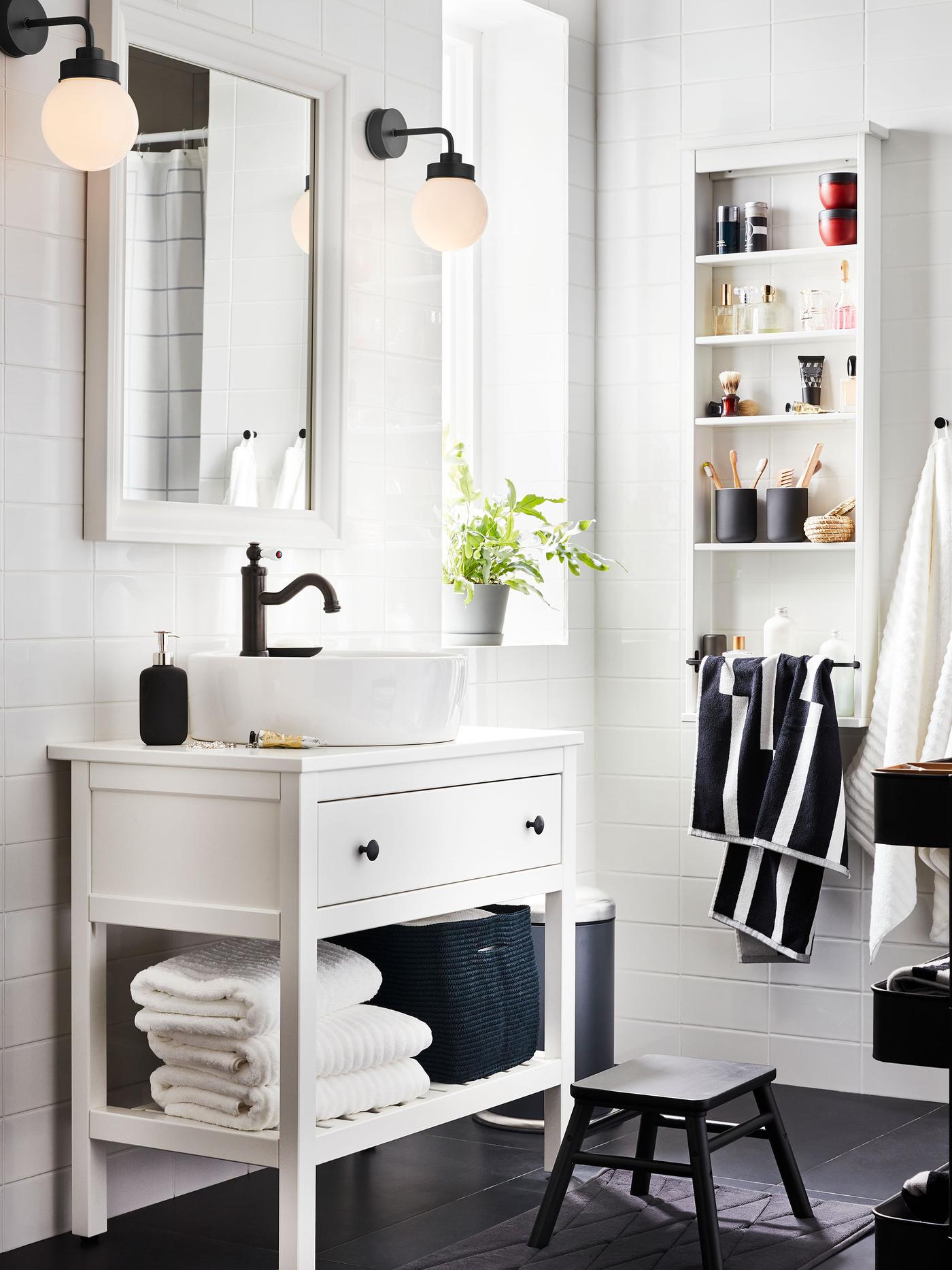 White HEMNES bathroom furniture with one drawer, one shelf with towels and a HAMNSKÄR mixer, a mirror, and two lamps.