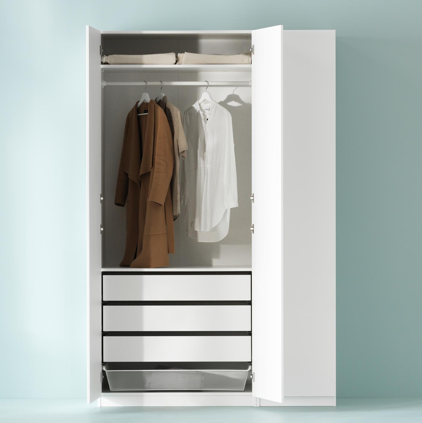 White PAX wardrobe against a light-green wall, two hinged doors open, shirts hang on a rail above drawers and a mesh basket.