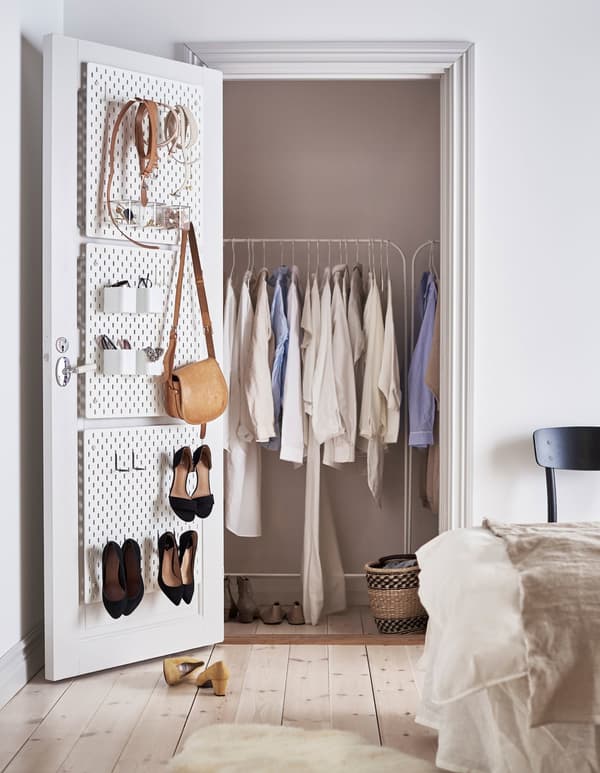 White SKÅDIS pegboards attached to the inside of a closet door to organize accessories and shoes