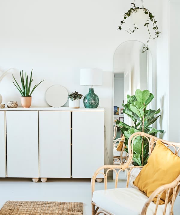 White stained cupboards with plants, a mirror and green lamp on the top, an arch-shaped mirror is framed by a hanging plant.