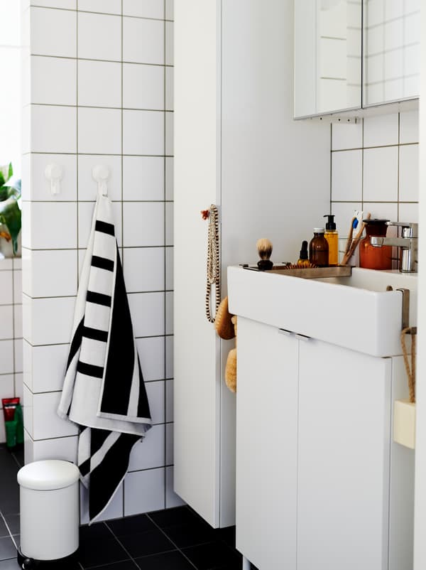 White-tiled bathroom furnished with white LILLÅNGEN cabinets and washbasin, and dotted with decorations and accessories.