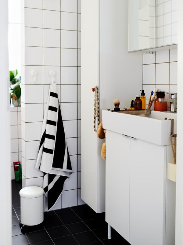 White-tiled bathroom furnished with white LILLÅNGEN cabinets and washbasin, and dotted with decorations and accessories.