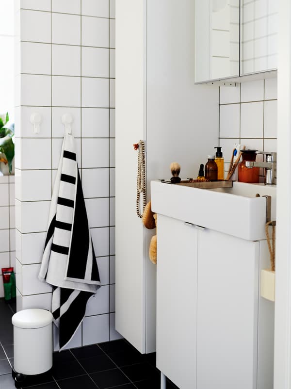White-tiled bathroom furnished with white LILLÅNGEN cabinets and washbasin, and dotted with decorations and accessories.