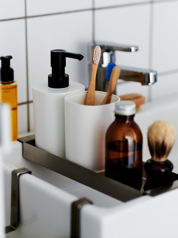 White-tiled bathroom interior with a slim rack placed across a LILLÅNGEN washbasin, holding a STORAVAN bathroom set.