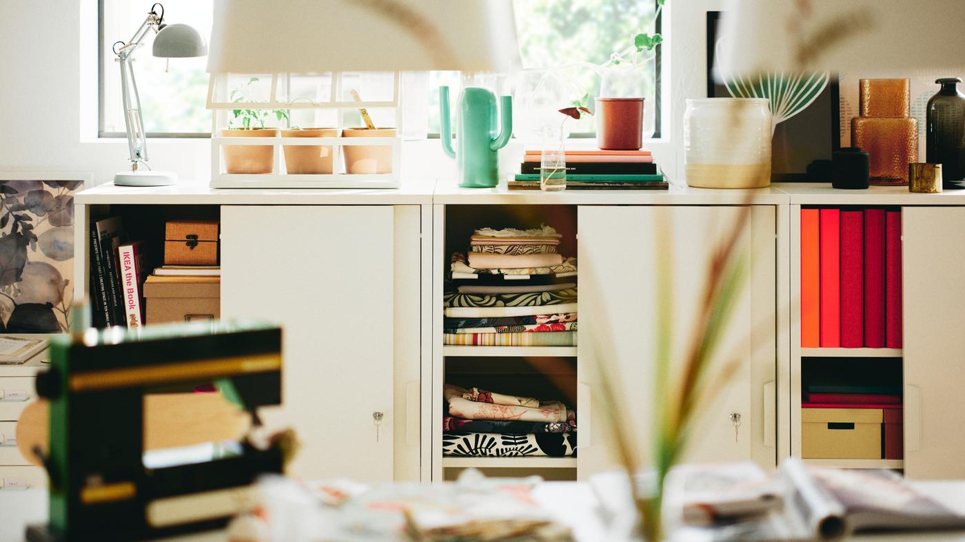 White TROTTEN cabinets with sliding doors with a bright green ÄRTBUSKE vase/watering can on top of one of them.