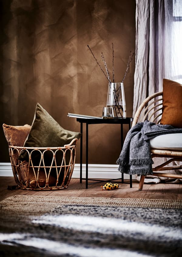 Wicker basket, standing on a stool in a living room, filled to the brim with different soft toy animals.
