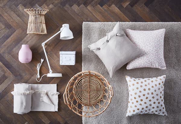Wicker baskets, pale coloured pillows and throws and a white work lamp displayed on a hardwood floor.